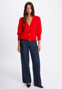 Rote Strickjacke mit tiefem V-Ausschnitt, gerippten Bündchen und fünf Knopfverschlüssen, kombiniert mit dunkelblaus weitem Hosen.