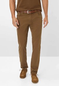 Pantaloni in cotone marrone chiaro con vestibilità dritta, abbinati a una cintura in pelle marrone con fibbia in argento, indossati con scarpe in suede beige.