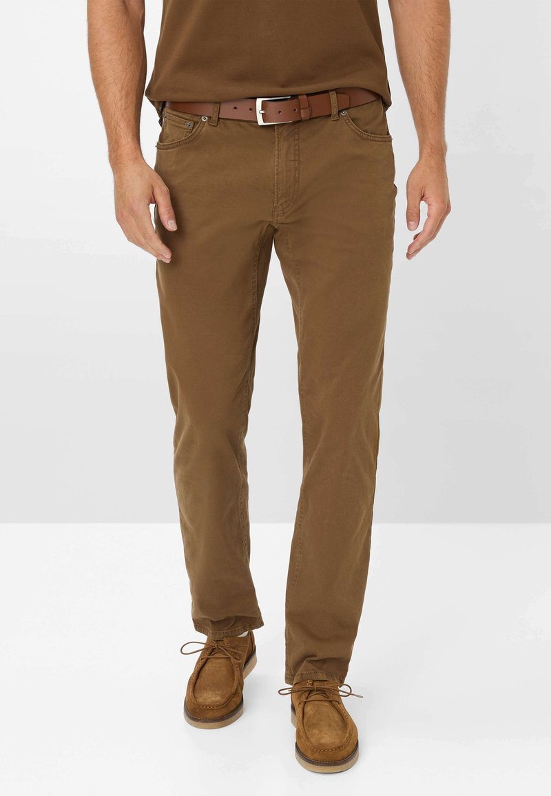 Pantaloni in cotone marrone chiaro con vestibilità dritta, abbinati a una cintura in pelle marrone con fibbia in argento, indossati con scarpe in suede beige.