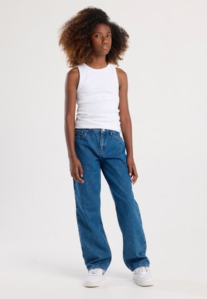 Canotta bianca senza maniche abbinata a jeans a palazzo a righe blu e sneakers bianchi. L'outfit presenta un fit rilassato e uno stile casual.