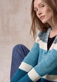 Stickad cardigan med horisontella ränder i nyanser av turkos, teal och vitt. Strukturerad tyg med knäppning.