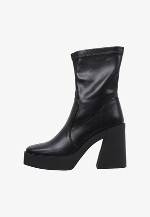 Bota de cuero negra hasta la mitad de la pantorrilla con un tacón ancho de bloque y suela plataforma, que presenta un detallado pespunte en el borde superior.