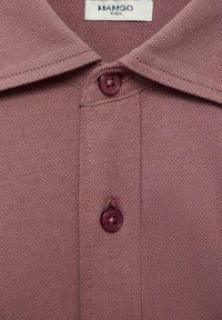 Primo piano di un colletto di una polo mauve testurizzato con due bottoni coordinati e un'etichetta Mango Kids all'interno della scollatura.