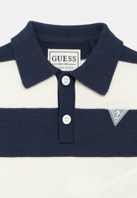 Ριγέ μπλε ναυτικό και λευκό πόλο μπλουζάκι από πλεκτό ύφασμα. Διαθέτει γιακά, δύο κουμπιά και τρίγωνο λογότυπο σε ταμπελάκι.