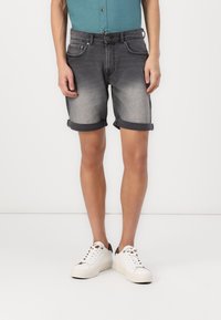 Jean-shorts i blekt grått med uppvikta kanter, med framfickor, bälteshällor och knäppning, kombinerat med vita sneakers.