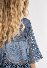 Top in pizzo all'uncinetto blu con maniche corte, dotato di un pannello posteriore testurizzato e ricami floreali. Design aperto e bordi scallop.