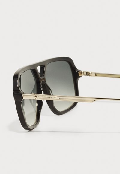 Svarta överdimensionerade solglasögon med gradientslinser, med en blank ram och guldmetallarmar graverade med varumärket.