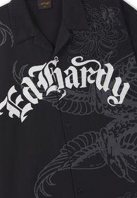 Black short-sleeve button-up shirt with white gothic "Ed Hardy" text and dark gray floral and winged graphic patterns.