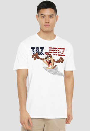 Young man wearing white T-shirt with cartoon Tasmanian Devil emerging from a tornado and text "TAZ FOR PREZ" in stars and stripes style.