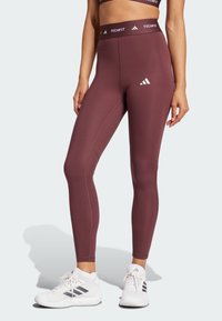 Leggings de sport bordeaux avec une taille haute et un logo de marque blanc. Texture lisse avec un design ajusté et des détails de couture subtils.