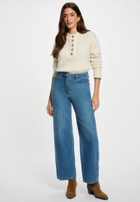 Maglione a coste color crema con bottoni, jeans blu a vita alta e gamba larga, e stivali chelsea marroni. Design semplice con una vestibilità comoda.