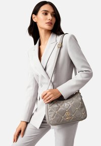 Borsa a tracolla in pelle verniciata grigia con finiture dorate, motivo trapuntato a rombi e borchie decorative. Tracolla regolabile per l'uso a tracolla.