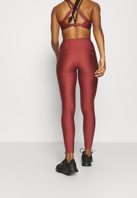 Bordeaux sport-bh met kruisbandsluitingen, gecombineerd met bijpassende hoog-getailleerde leggings. Beide hebben een soepele textuur en een strak ontwerp.