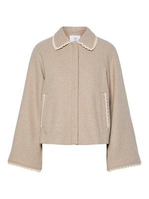 Veste en laine beige avec un col en vagues, des poches avant et de larges manches évasées. Présente un tissu texturé et des accents de dentelle contrastants.