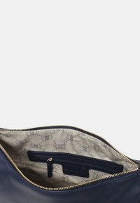 Navy leren tas met een gouden ritssluiting, met een gestreepte beige binnenvoering en een ritsvak tegen een gladde textuur.