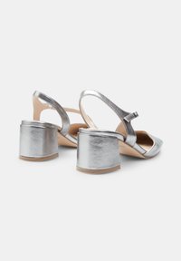 Silver metallic slingback heels with a rounded toe, adjustable ankle strap, and chunky block heel. Smooth texture and minimalist design.