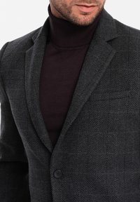 Mörkgrå hundtandsmönstrad blazer med slagkrage, enkel knappstängning och skräddarsydd passform, kombinerad med en figurnära mörk högkrage.