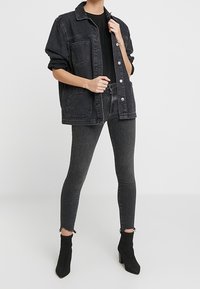 Black denim jacket with two front pockets, paired with dark skinny jeans. Tall black ankle boots with a pointed toe.