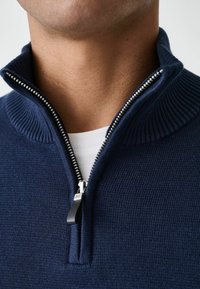 Marineblaues Zip-Pullover aus gerippter Strickware. Mit hohem Kragen und silbernem Reißverschluss mit schwarzem Zipper. Leicht strukturierte Oberfläche.