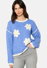 Sininen neulepaita, jossa on valkoisia kukkakoristeita. Ominaisuuksiin kuuluu pyöreä kaula-aukko, erottuva kantti sekä resoroitu rakenne hihoissa ja helmassa.