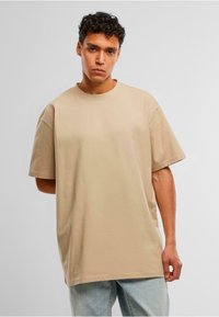 Beige oversized t-skjorte laget av bomull, med rund hals, korte ermer og en avslappet passform. Kombinert med lyseblå denimjeans.