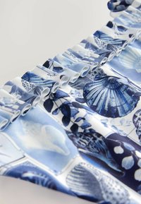 Blå och vit tyg med ett snäckmönster. Volangkanter skapar textur, med detaljerade illustrationer av snäckor och botaniska element.