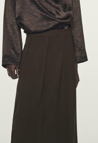 Gonna lunga marrone scuro in tessuto morbido e con design plissettato. Abbinata a un top lucido scuro con maniche lunghe e vestibilità rilassata.