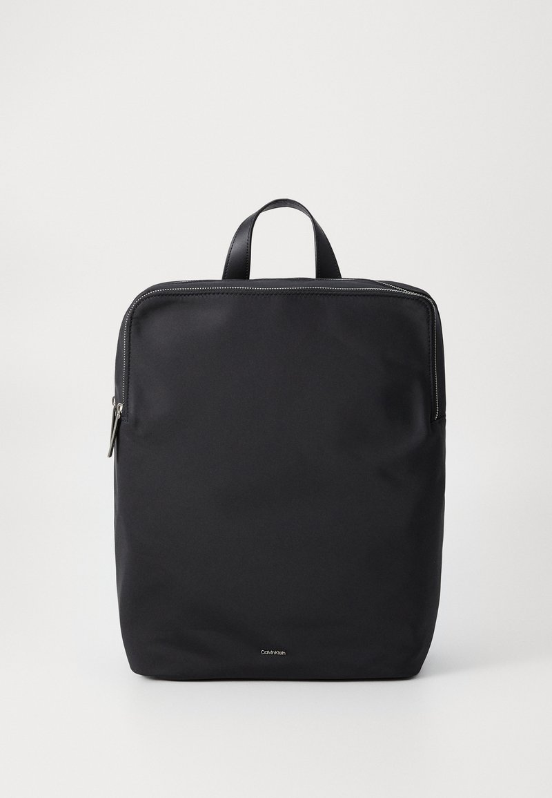 Zaino in nylon nero con un design minimalista, forma rettangolare, maniglia superiore e dettagli in zip argentati. Esterno semplice, senza motivi visibili.