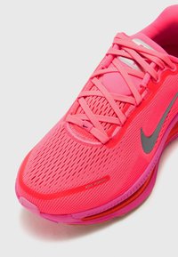 Chaussure de course Nike d'un rose vif avec une tige en mesh respirant, un bout arrondi et un logo swoosh gris. Elle présente des lacets texturés et un col rembourré.