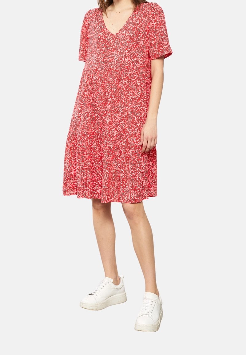 Robe florale rouge à manches courtes, décolleté en V, design à volants et tissu léger ; associée à des baskets blanches.