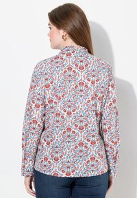 Camisa de manga larga con un patrón floral multicolor en rojo, azul y blanco, confeccionada en tejido ligero y con un diseño de alto cuello.