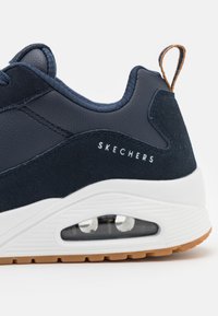 Navy blue sneaker with a smooth leather and suede upper, white midsole, textured rubber outsole, and a visible air unit. Brand logo on side.