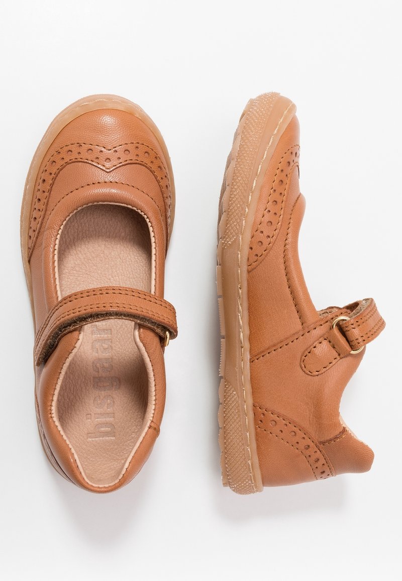 Zapatos de cuero marrón con punta redondeada, acentos perforados y una correa de Velcro. Suela de goma flexible con un patrón texturizado.