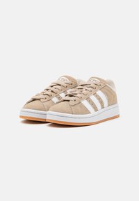 Beežid suedesneakerid valgete triipudega, ümmarguse varbaga, lamedate kummitaldadega ja sidumisdisainiga. Omavad äärtes õmblust üksikasju ja logo aktsente.