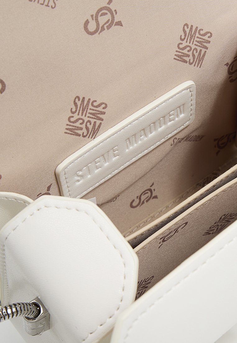 Innenleben einer weißen Kunstlederhandtasche mit beiger Fütterung, die ein wiederholendes "SM"-Logo-Muster aufweist, sowie einem eingeprägten Markenetikett in der Tasche.