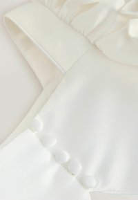 Valge satiinist kleit rippuva kaeluse ja külgse rida kangast kaetud nööpe, esitledes sujuvat, tekstuuri viimistlust.