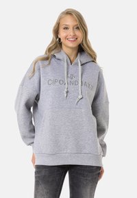 Grauer Hoodie mit einer Vordertasche, Kapuze mit Kordelzug und gesticktem Logo. Verfügt über eine lockere Passform und weichen Stoff, kombiniert mit dunklen Jeans.