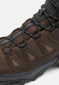 Brązowe buty outdoor z siateczkową cholewką, gumową podeszwą i nakładkami TPU. Posiada czarne sznurowadła i wyraźne wzory trzymania na podeszwie.