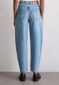 Lyseblå denimbukser med høy midje, brede ben og baklommer. Har en merket lærlapp i livet og oppbrettede hem.