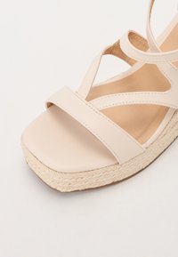 Beige espadrille-inspirert sandal med en glatt faux lær øvre, kryssbånd og en vevd jute plattform såle.