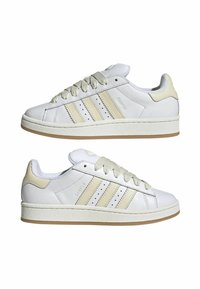 White leather sneakers with cream accents, textured sole, and three lateral stripes. Features round toe and flat laces.