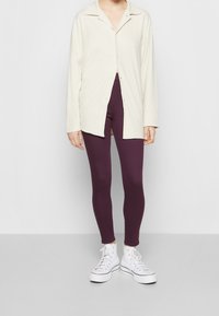 Krämfärgad skjorta med långa ärmar, kombinerad med figurnära lila tights och vita hög-top sneakers. Slät textur, avslappnad passform.