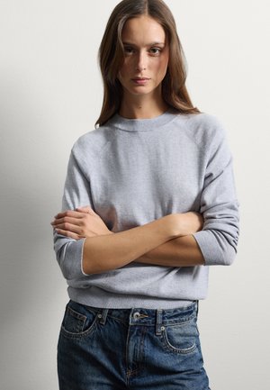 Grijze gebreide trui met een geribbelde kraag en manchetten, voorzien van een relaxed fit en een zachte textuur, gecombineerd met blauwe denim jeans.