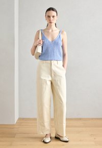 Lyseblå strikket tanktop med V-hals, beige vide bukser og kremfargede tøfler med svarte detaljer; minimalistisk design og tekstur.