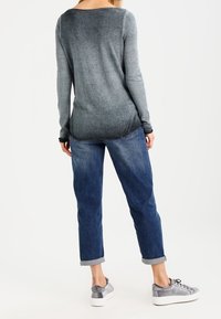 Långärmad tröja i gradientgrått med rundad halsringning, kombinerad med uppvikta ärmar, blå denimjeans och grå sneakers. Mjuk textur synlig.