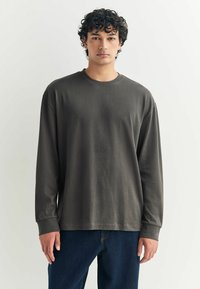 Długi rękaw, ciemnoszary T-shirt wykonany z miękkiej bawełny. Posiada okrągły dekolt i luźny krój. Noszony z ciemnymi dżinsami, minimalne detale.