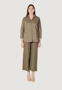 Camicia verde oliva con bottoni e maniche lunghe, abbinata a pantaloni a gamba larga verde oliva. Tessuto liscio con design minimalista e senza motivi.