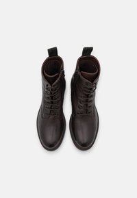 Bottes basses en cuir marron avec bout rond, laçage à l'avant et deux languettes. Texture lisse et coutures minimales visibles.