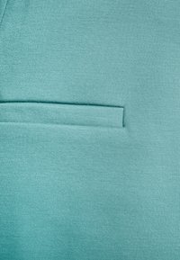 Turquoise fabric with a textured finish featuring a small, horizontal pocket integrated into the design. Smooth and structured appearance.