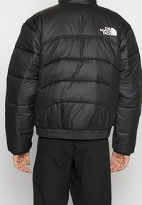 Osoba w czarnej, ocieplanej kurtce North Face, pokazująca tył z logo na górnej prawej stronie, w połączeniu z czarnymi spodniami.